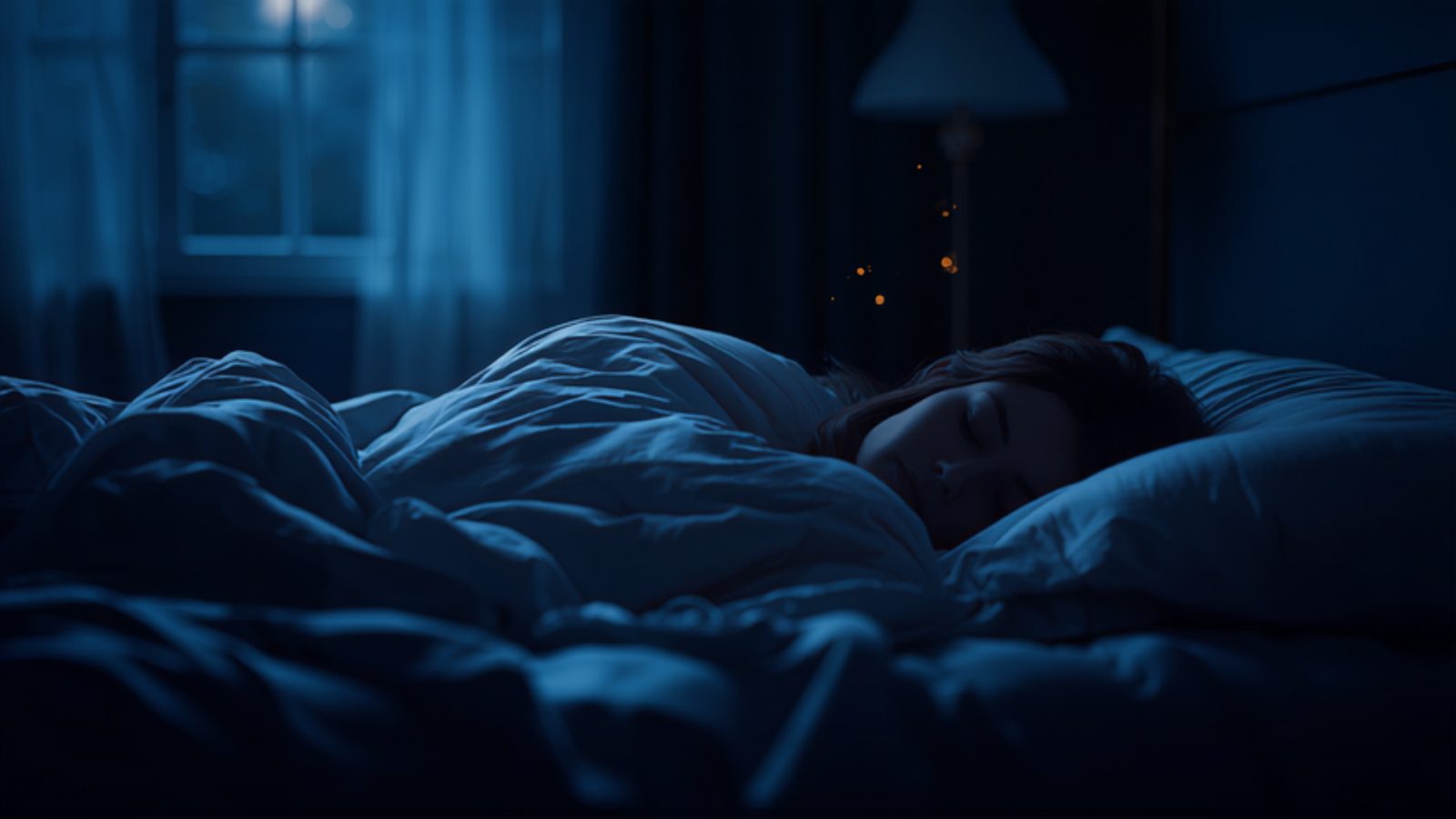A person sleeping peacefully under a duvet in a dark blue bedroom with faint points of light near the bed suggesting sleep sensors